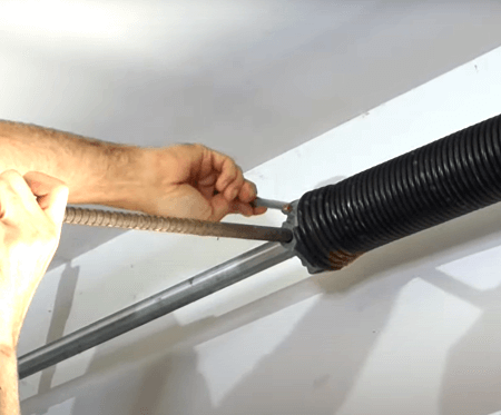 A person is fixing a garage door spring with a screwdriver.