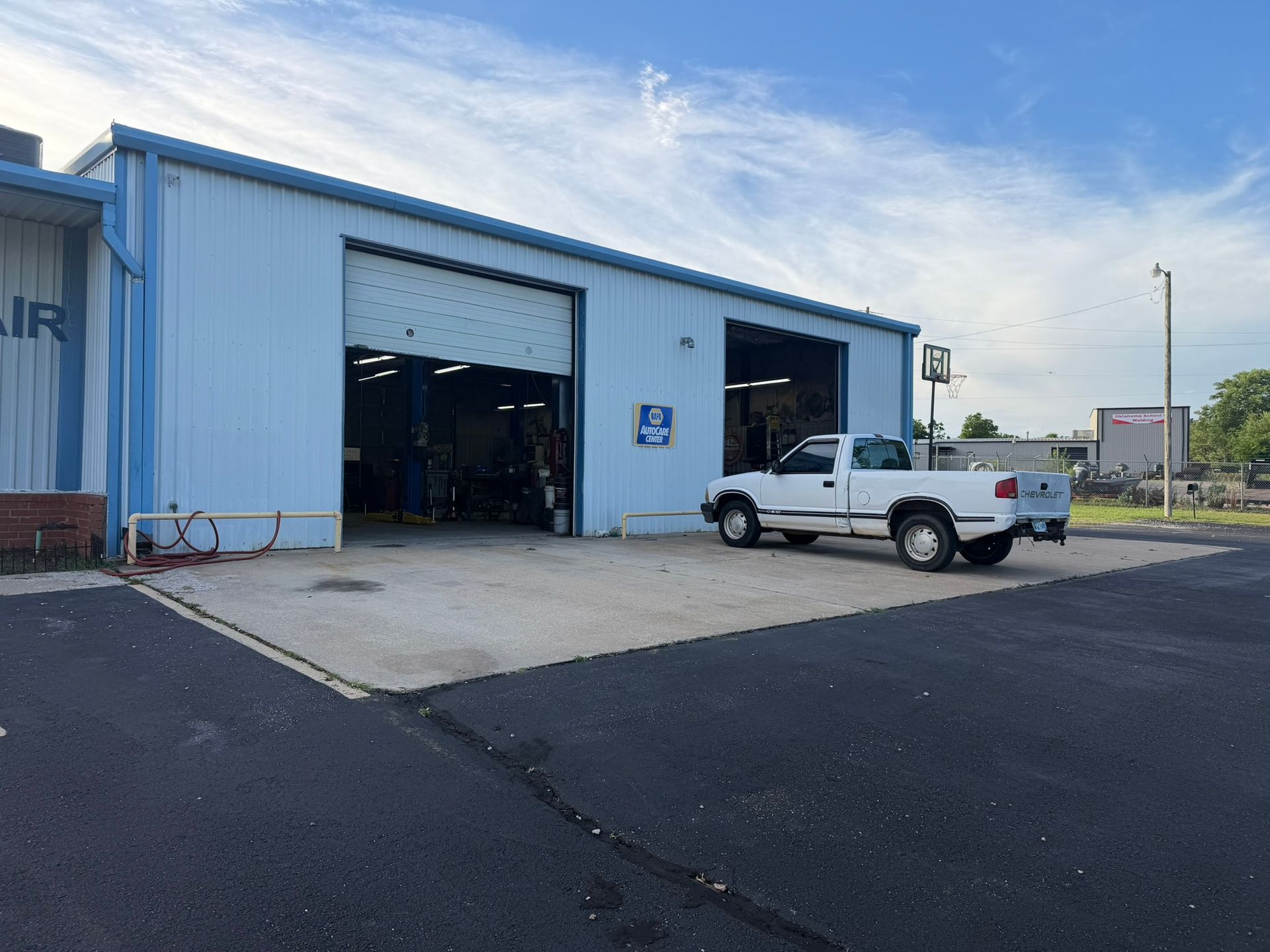 White pickup truck outside a blue industrial garage with open bay doors and asphalt lot