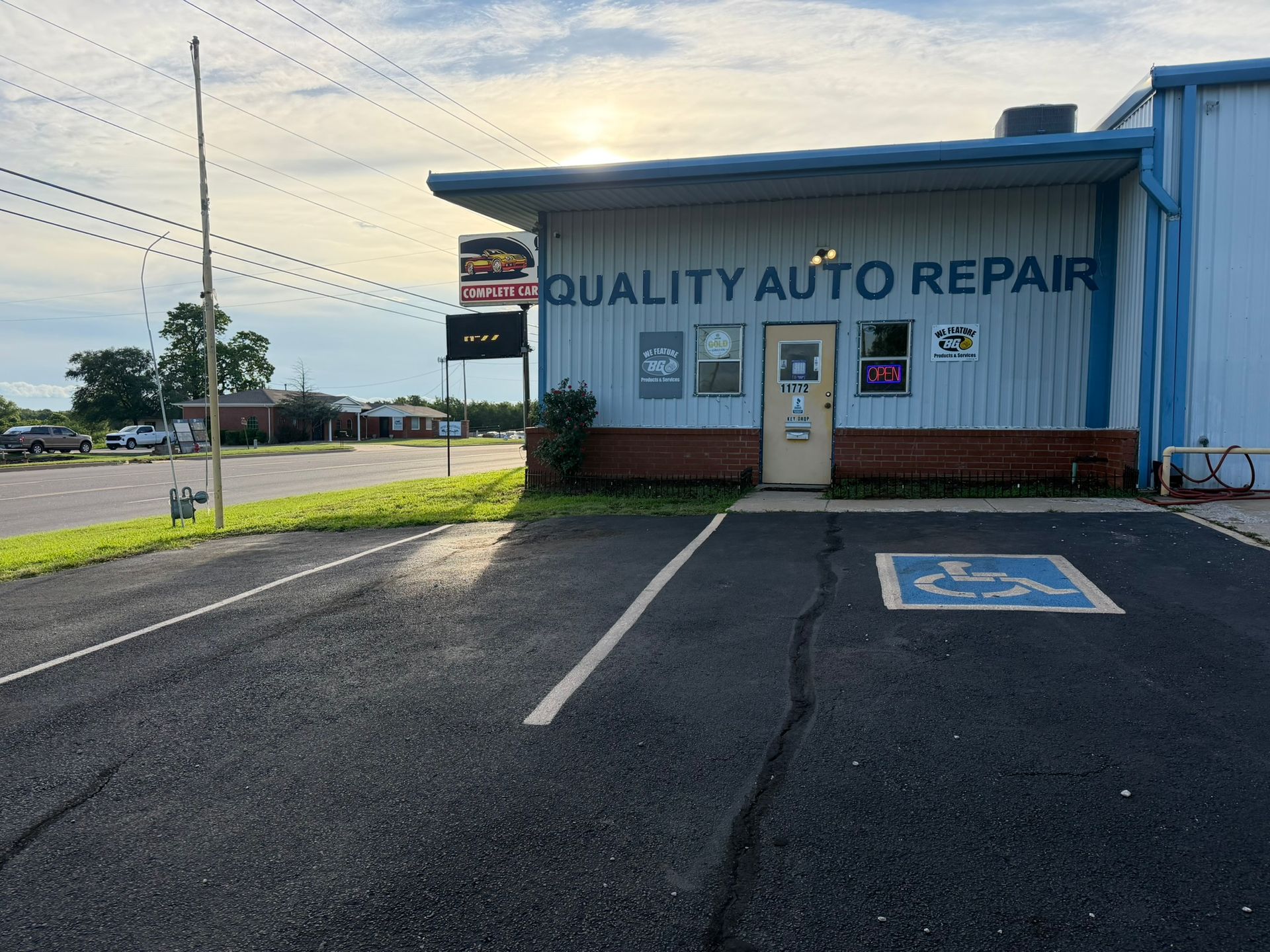 Small auto repair shop with blue siding, parking lot, and accessible parking space at sunset.