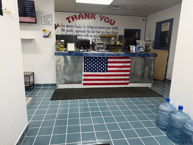 Small lobby counter with a large American flag and a “Thank You” sign, blue tiled floor, and water jugs.