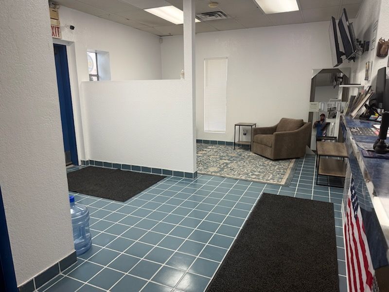 Empty office interior with blue tiled floor, black mats, white walls, and a brown chair in the back.