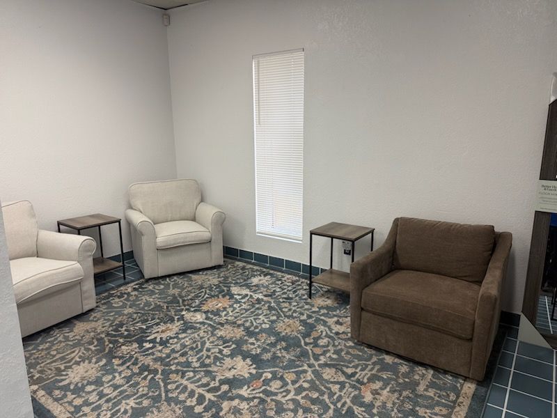 Small living room with beige and brown armchairs, side tables, and a patterned blue rug.
