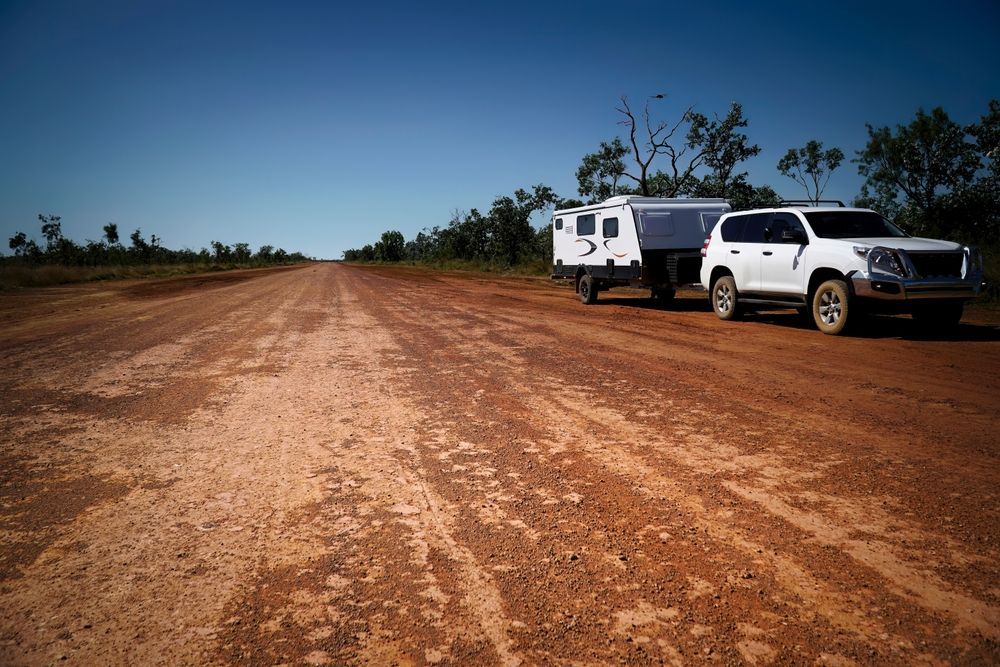 White SUV Towing a Camper Trailer on a Red Dirt Road Under a Clear Blue Sky — Total Caravan Repairs in Nabiac, NSW