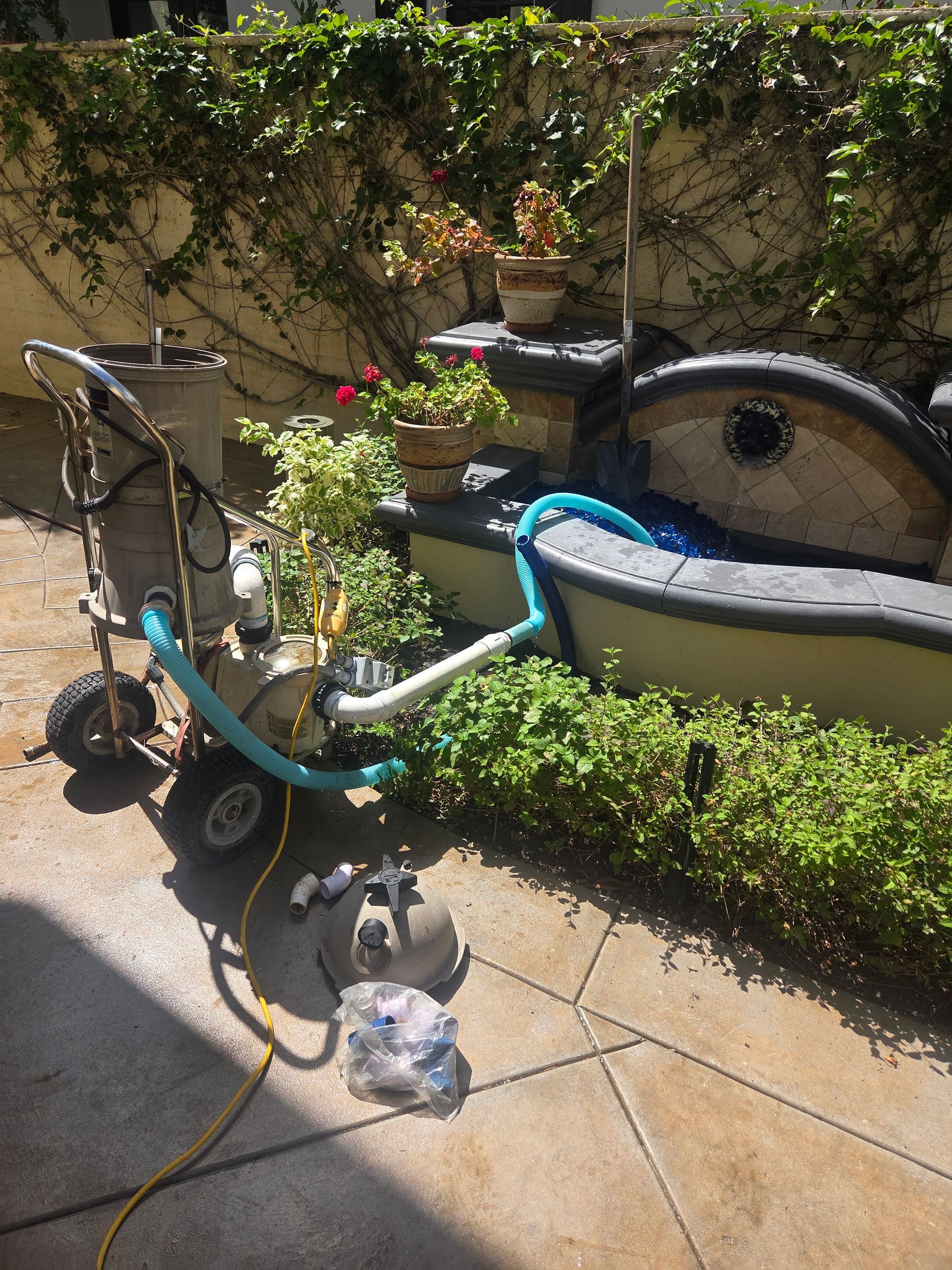 Turquoise bicycle parked beside a garden fountain and hedges on a sunlit patio.