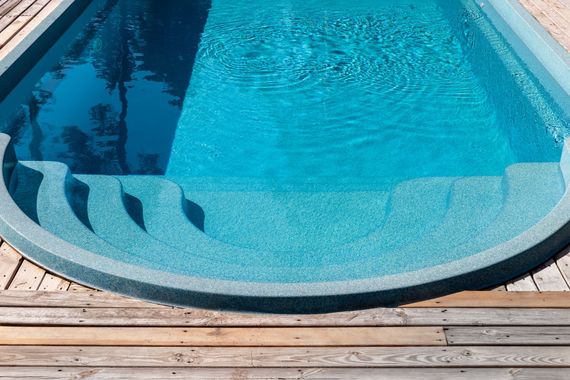 Curved backyard swimming pool with clear blue water and wooden deck