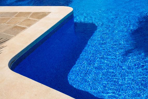 Blue swimming pool edge with sunlit water and beige tile deck