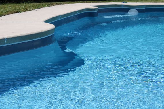 Blue swimming pool with curved white deck edge and clear water reflections