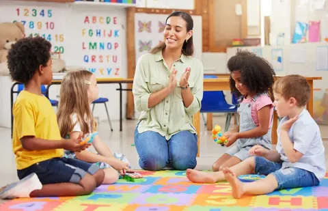 A teacher is sitting on the floor talking to a group of children.