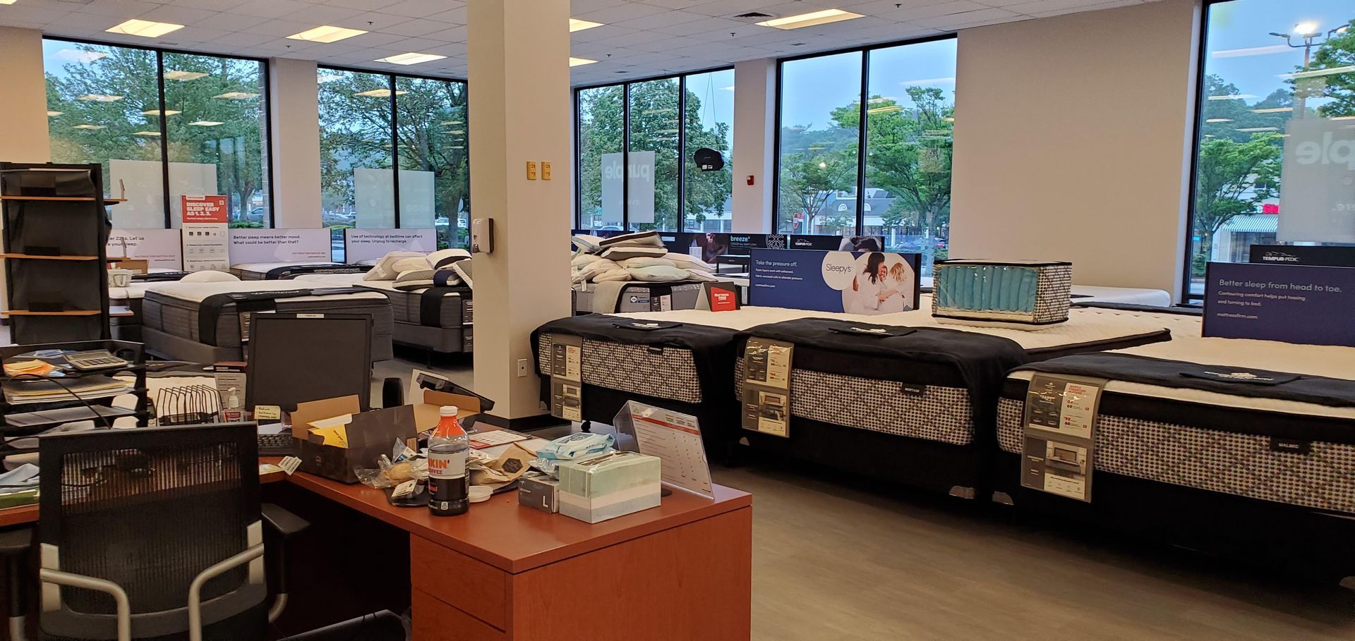 Office interior with desks, chairs, and large windows overlooking trees.