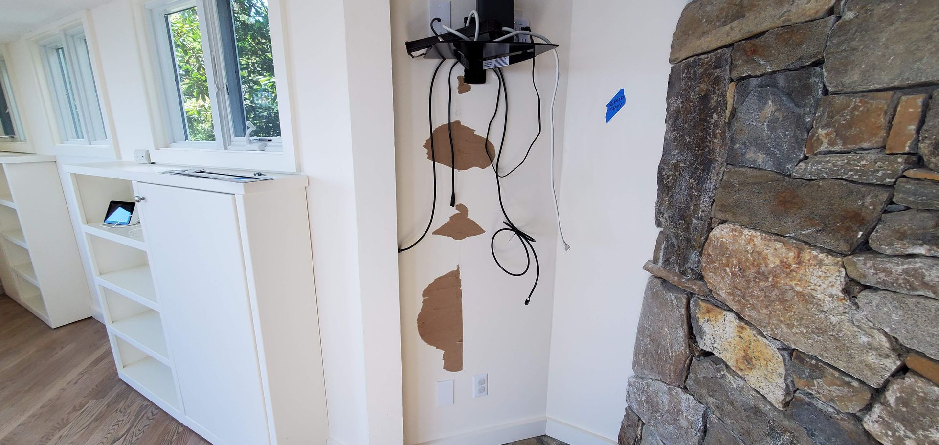 White shelves by a window with exposed wiring and stone fireplace.