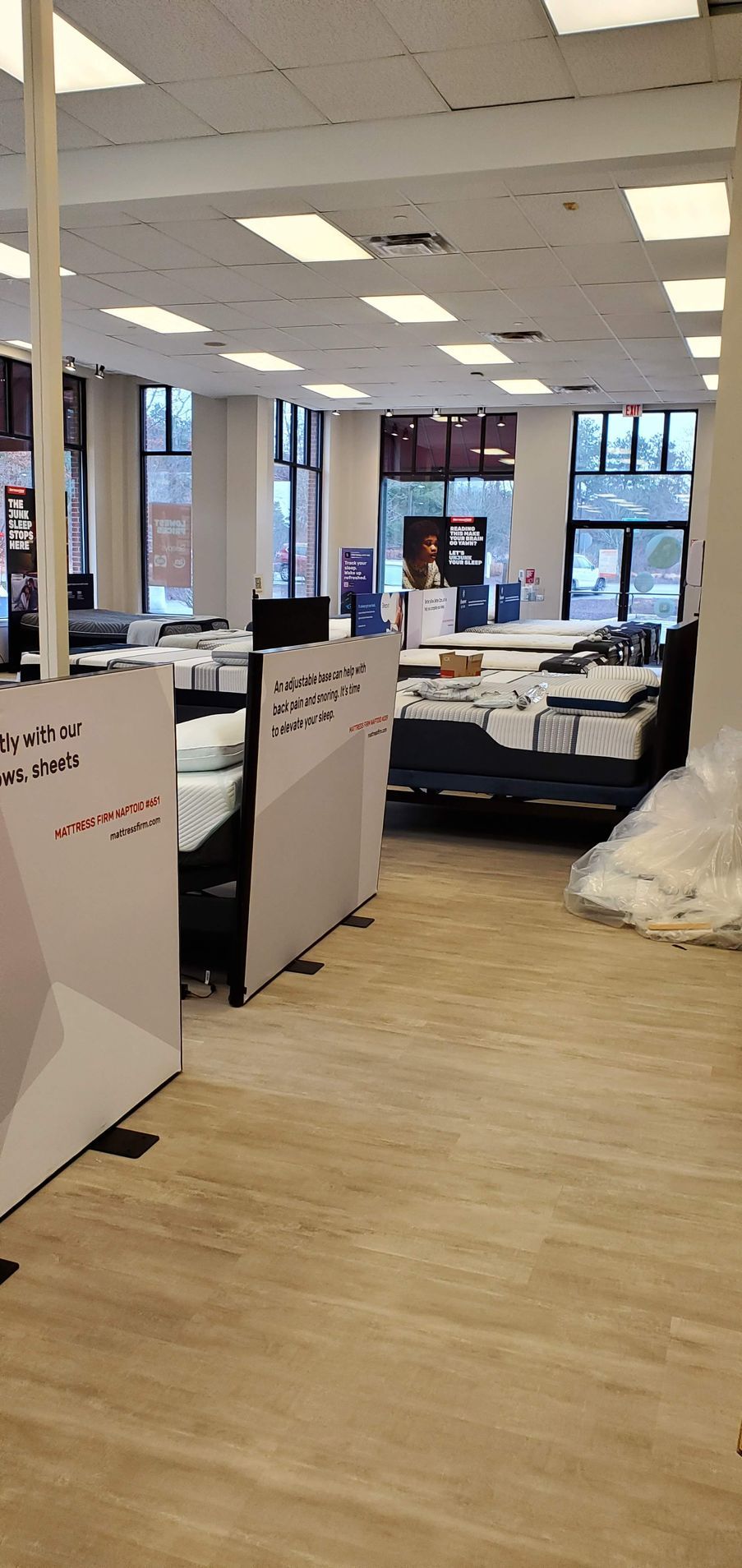 Interior of a store or office with white dividers, showing bedding display, fluorescent lighting, and windows.