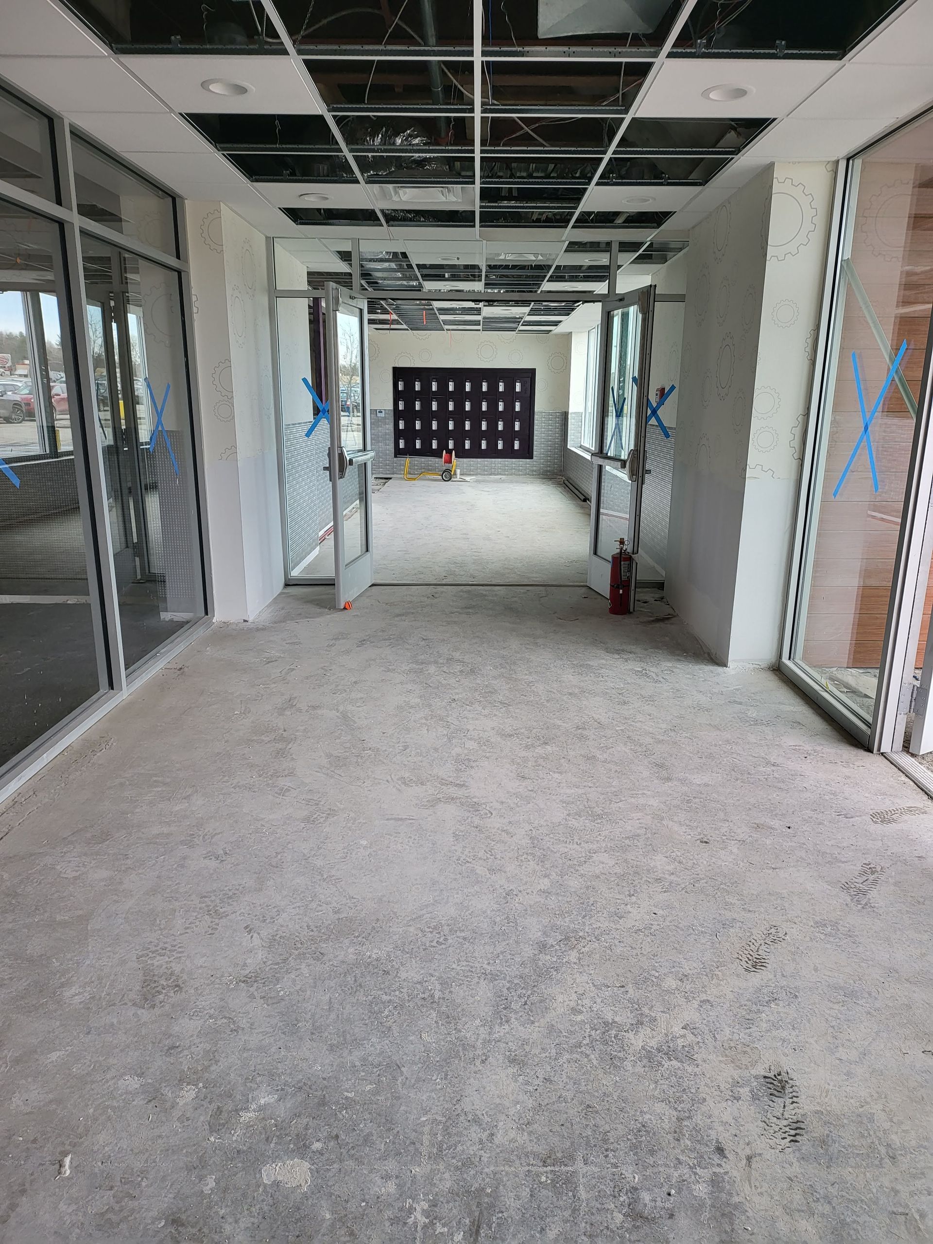 Construction hallway, unfinished ceiling, concrete floor, glass doors, and entrance to a room.