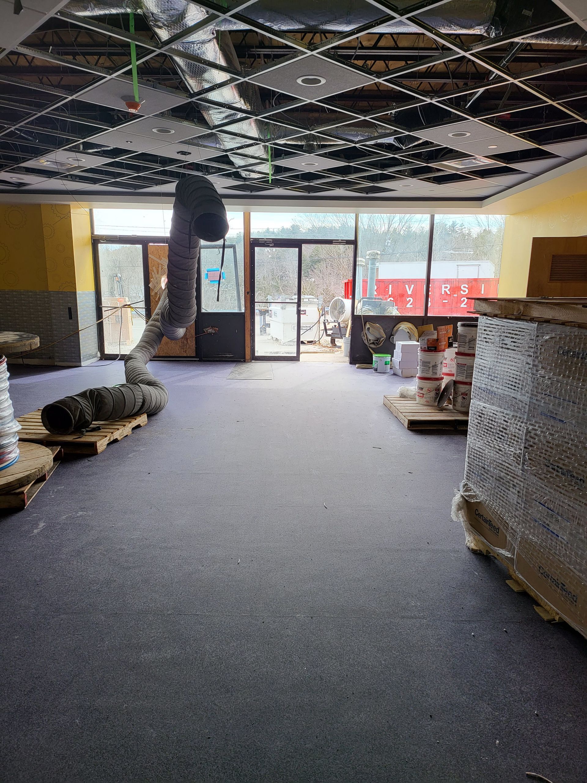 Empty interior with reflective ceiling, large windows, and gray carpet.