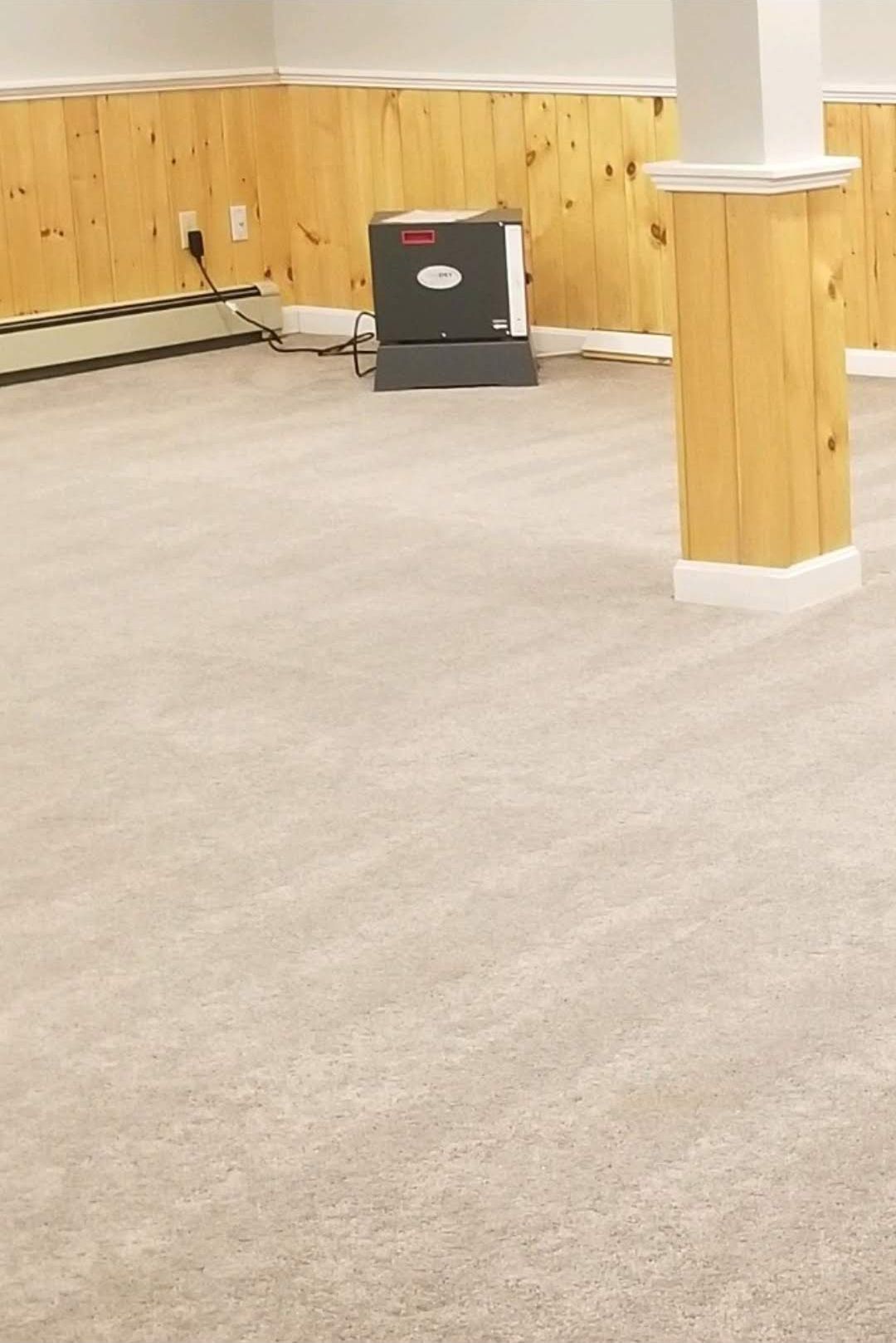 Empty room with beige carpet, wooden paneling, and a support column.