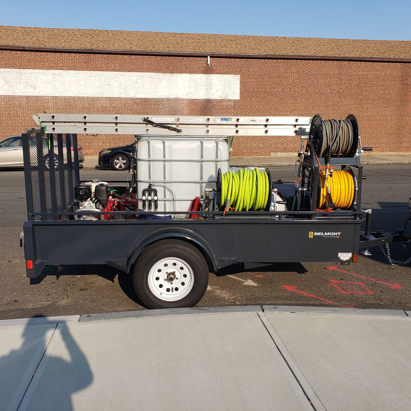 A trailer with hose reels on the back is parked in front of a brick building