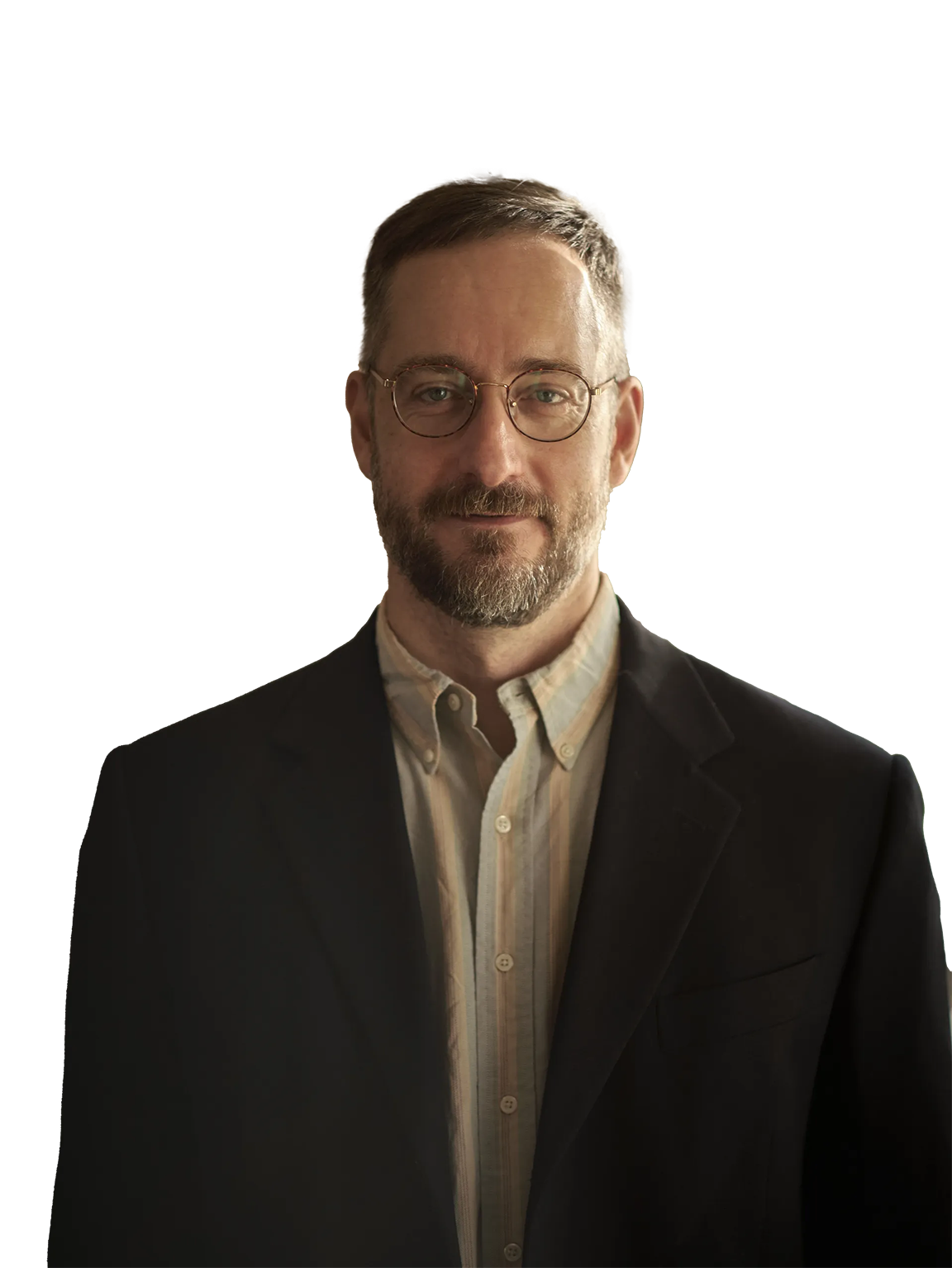 A man with short hair and glasses, wearing a light collared shirt and dark blazer, stands against a plain white background.