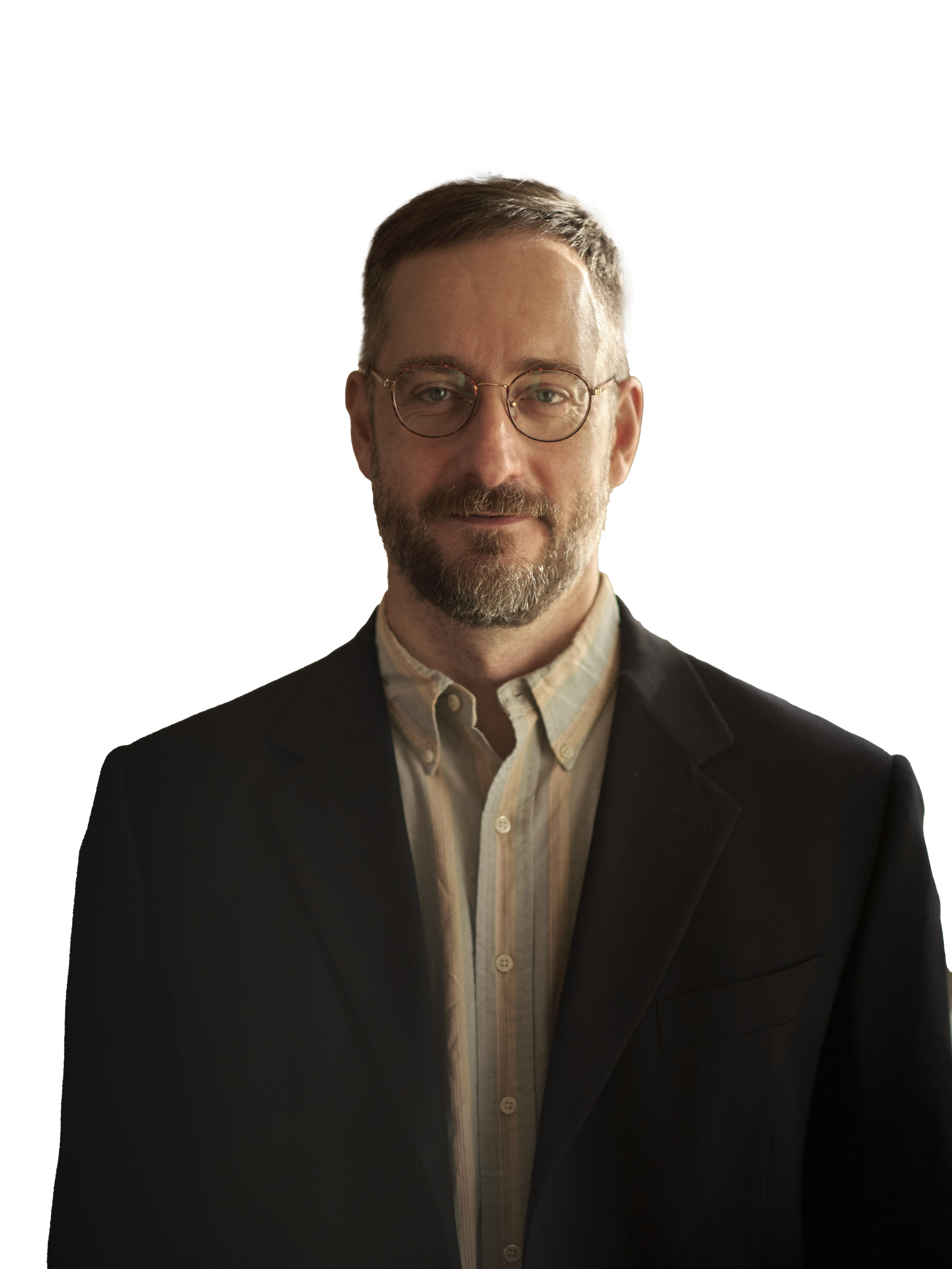 A man with short hair and glasses, wearing a light collared shirt and dark blazer, stands against a plain white background.