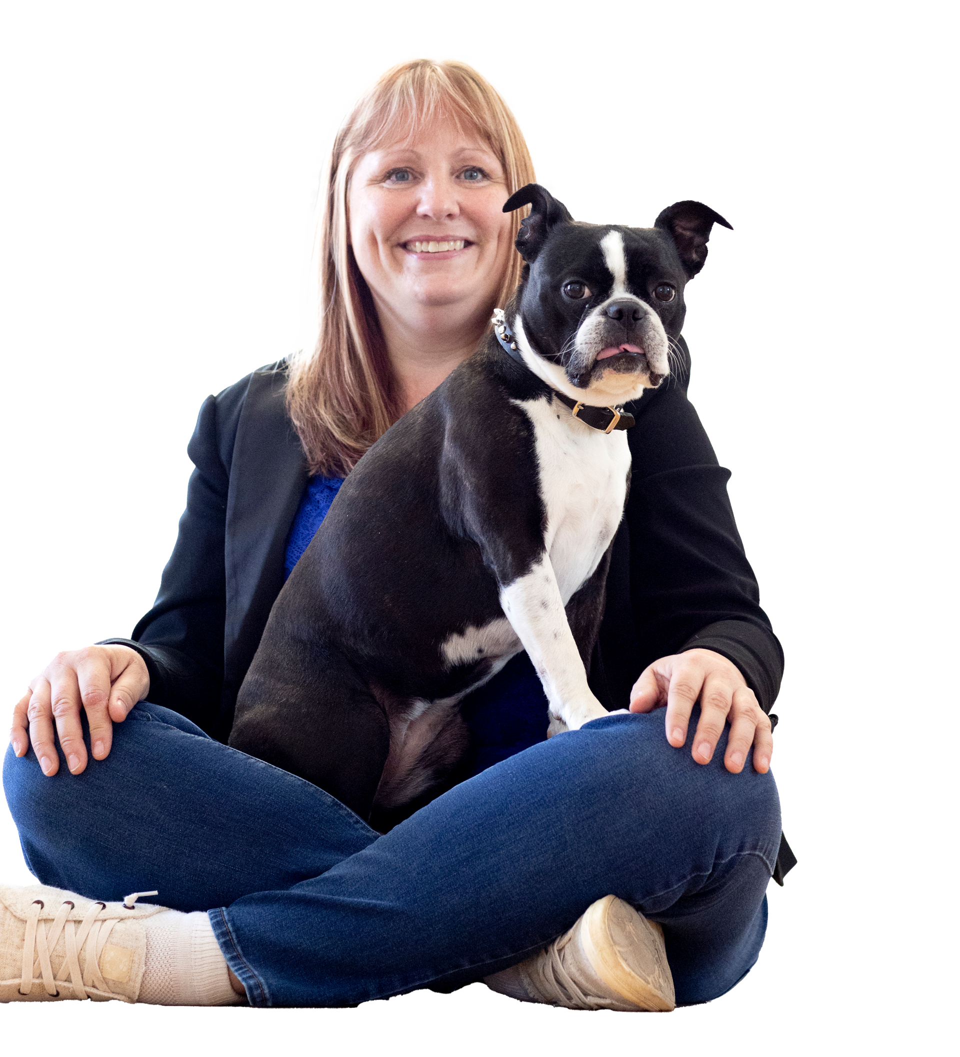 A person sitting cross-legged on the floor, smiling while holding a black and white Boston Terrier.