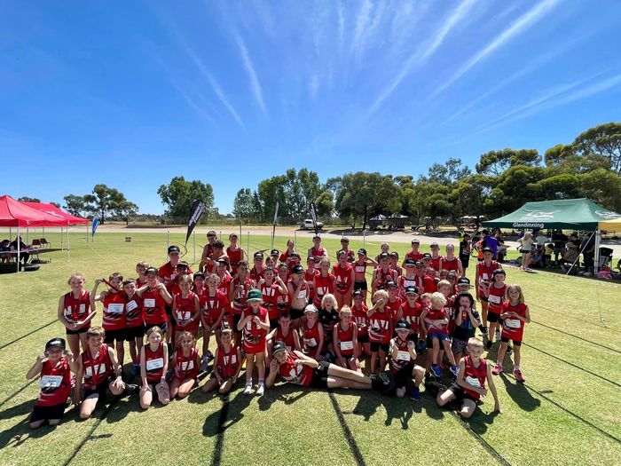 Large group of runners in red uniforms pose on a grassy field under a blue sky.