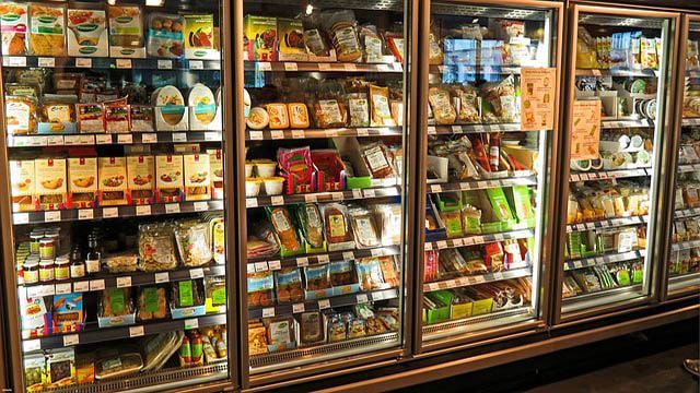 A row of refrigerators filled with lots of food in a grocery store.