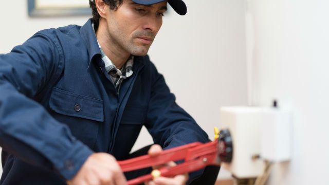 A man is sitting on the floor fixing a pipe with a wrench.