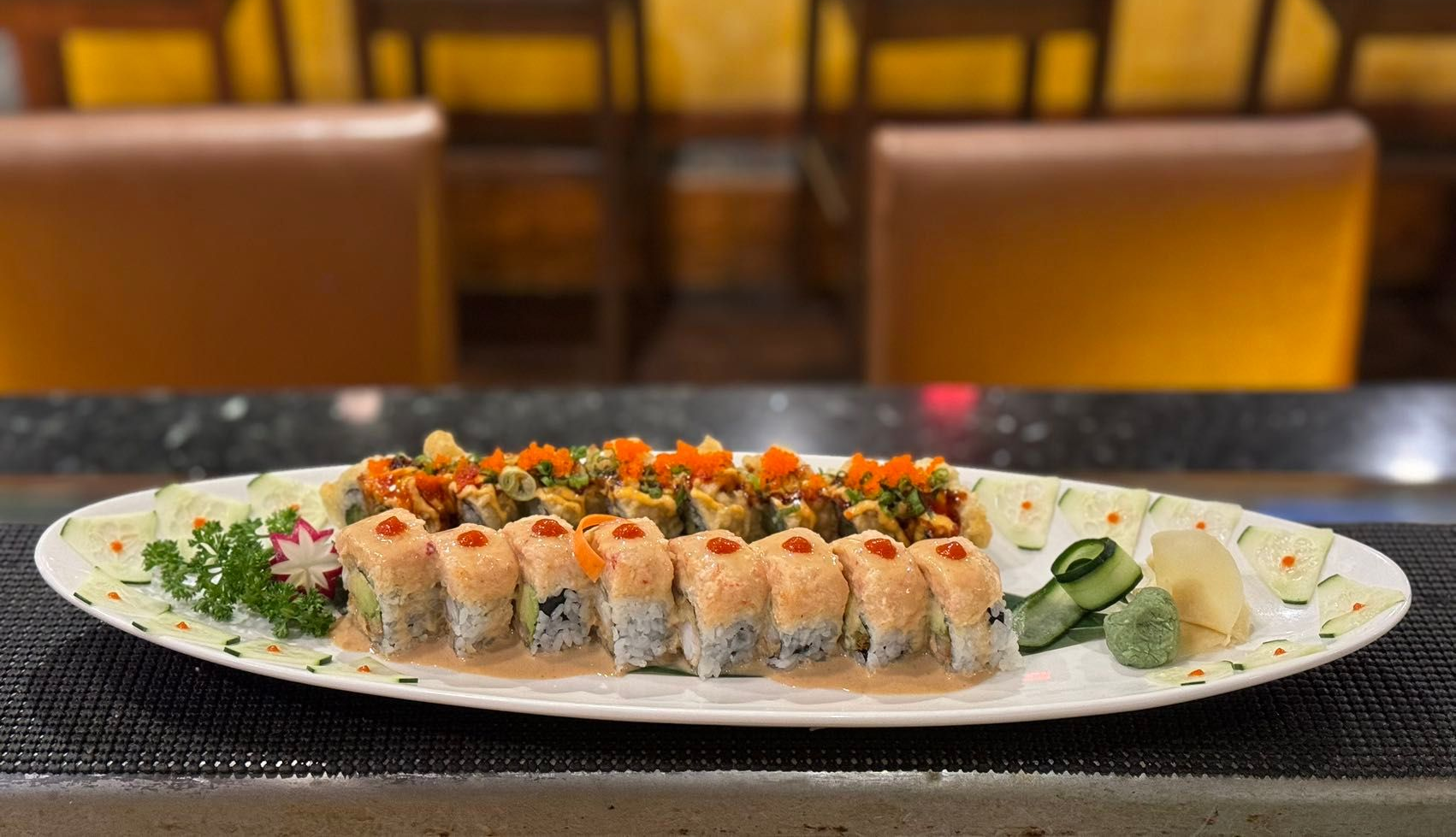 Sushi rolls on an oval plate with garnishes, set on a dark counter, restaurant background.