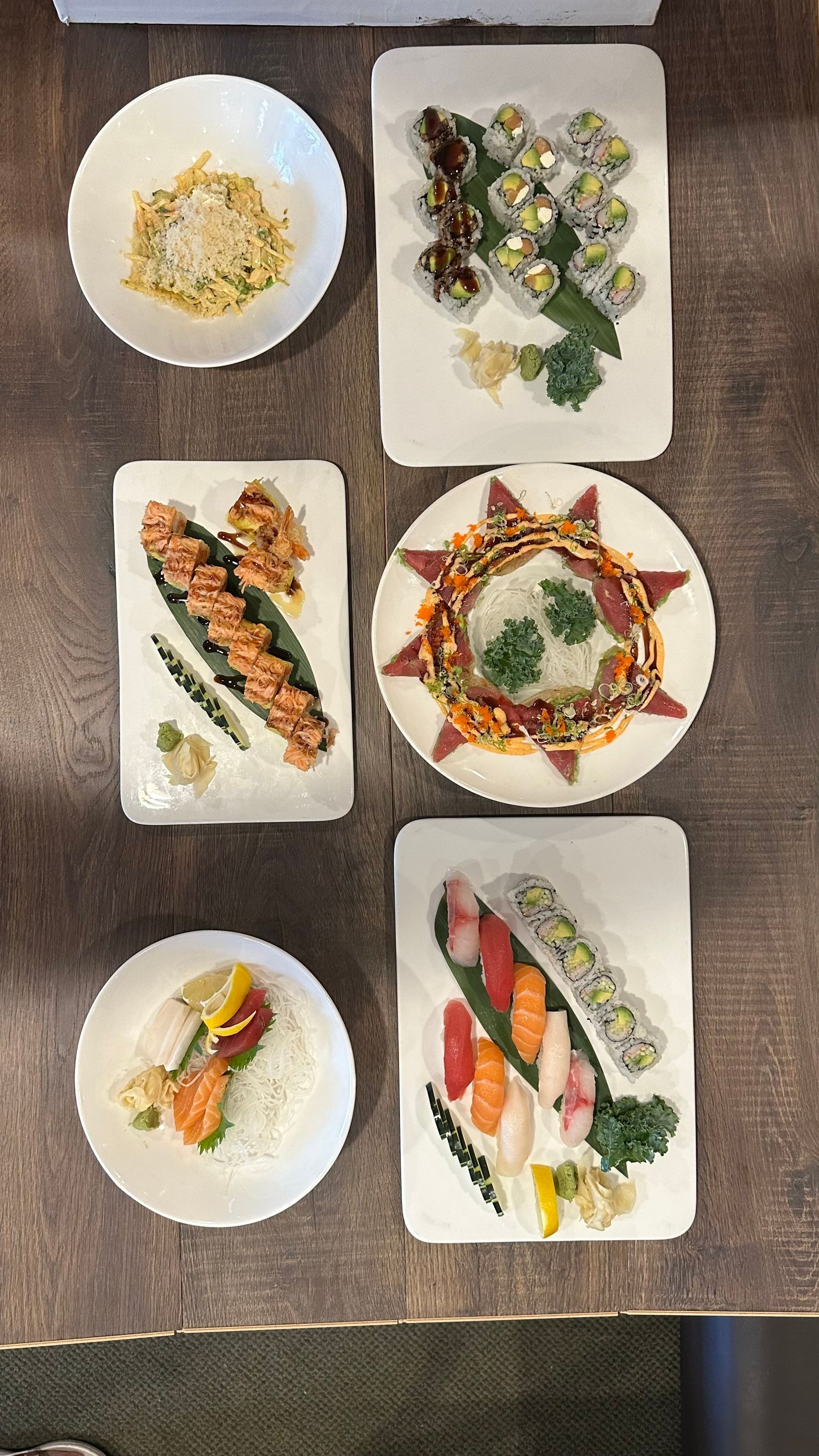 Sushi dishes on a dark wooden table, featuring rolls, nigiri, and rice bowls.