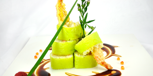 Sushi rolls with a green wrap, stacked on a plate with sauce and garnish.