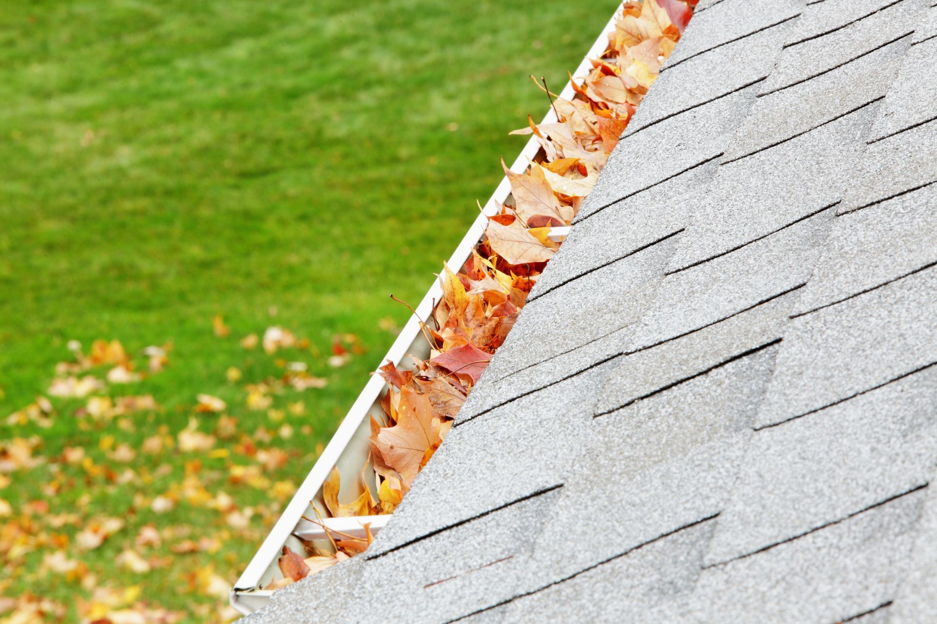 A Gutter Filled With Leaves On A Roof With A Lawn In The Background – Lincoln, NE – Gutter Cleaning and Repair
