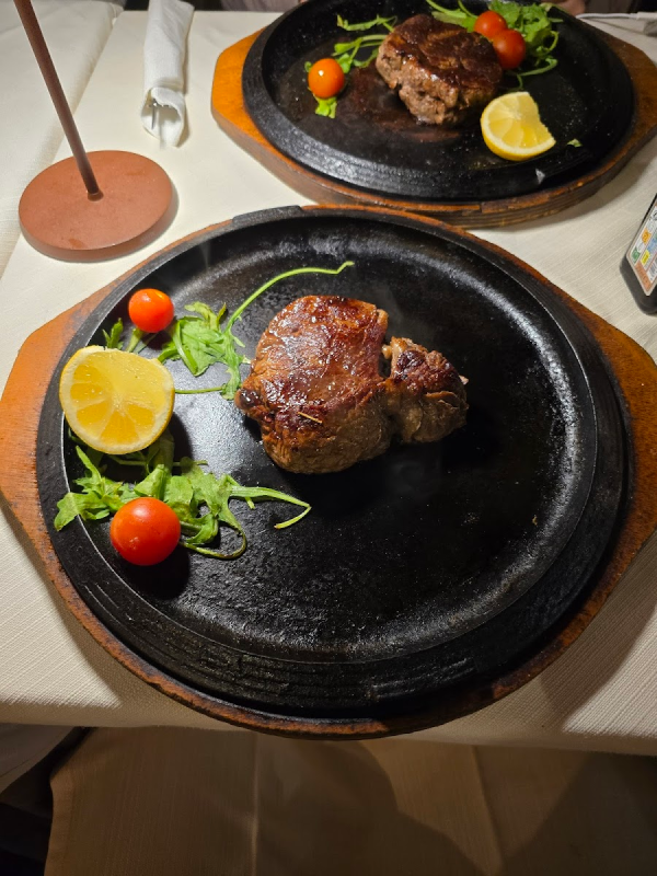 Due bistecche cotte su piatti neri con limone, pomodori e rucola.