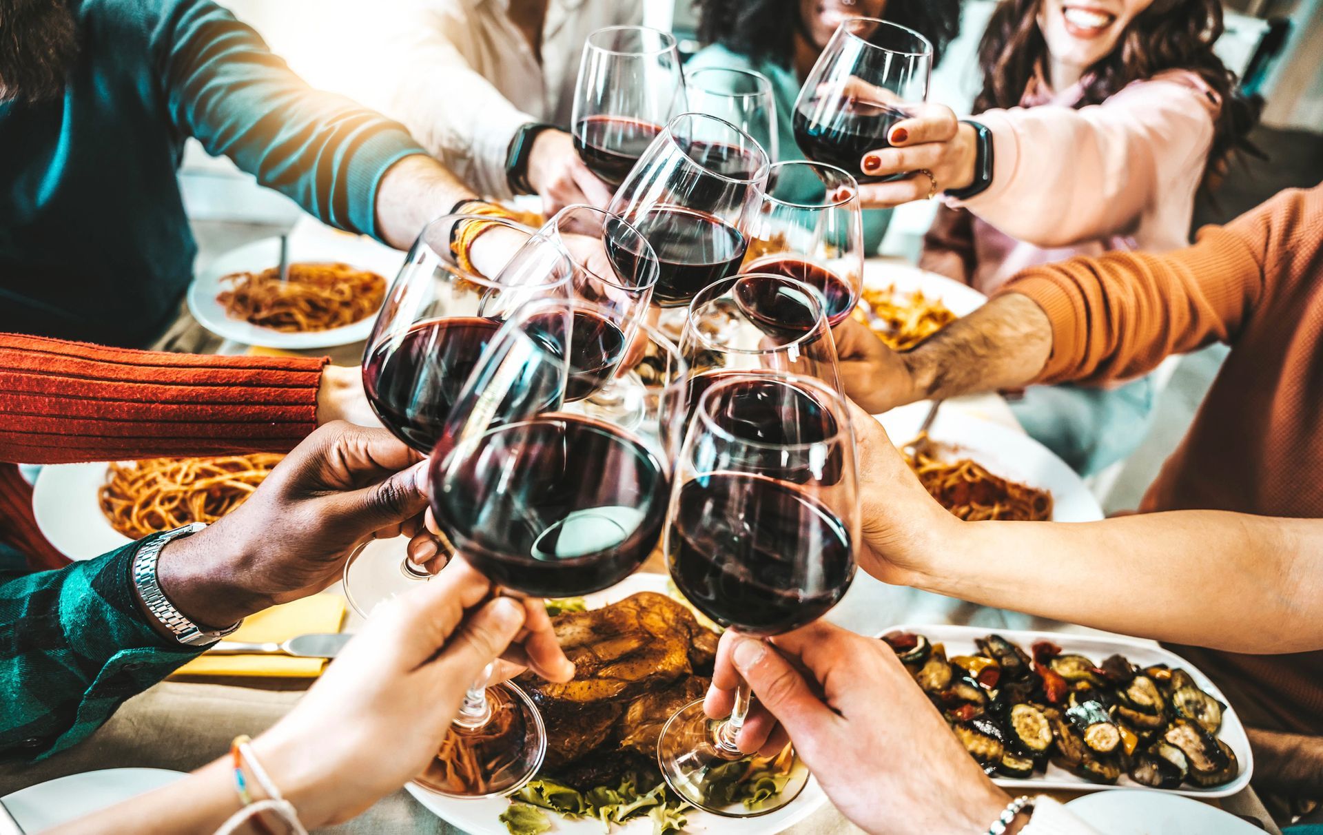 Persone che brindano con bicchieri di vino rosso su un tavolo imbandito.