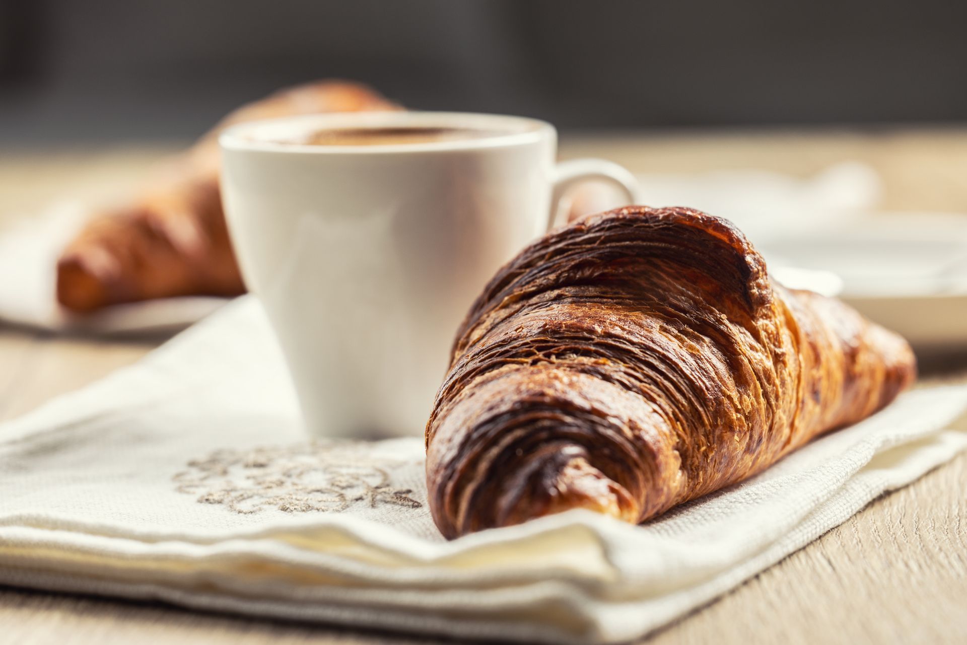 Cornetto e caffè in una tazza bianca su un tovagliolo bianco, tavolo di legno.