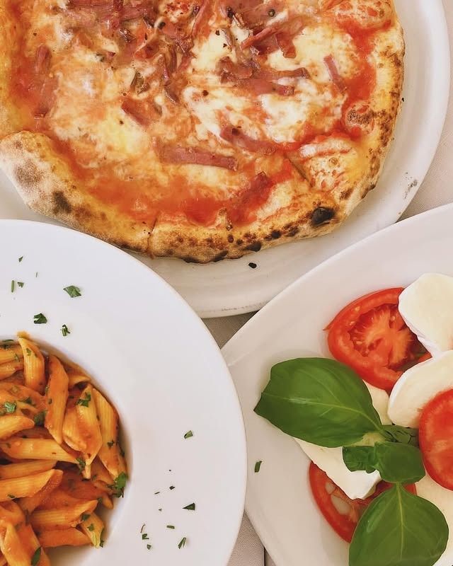 Pizza, pasta e insalata caprese su piatti bianchi.