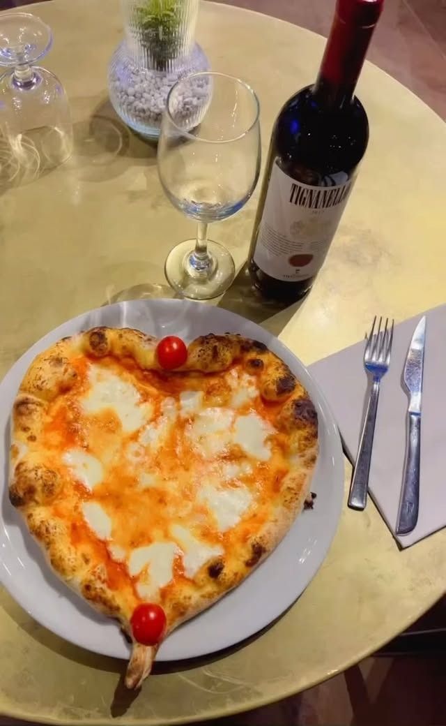 Pizza a forma di cuore con mozzarella, vino e un bicchiere, posta su un tavolo.
