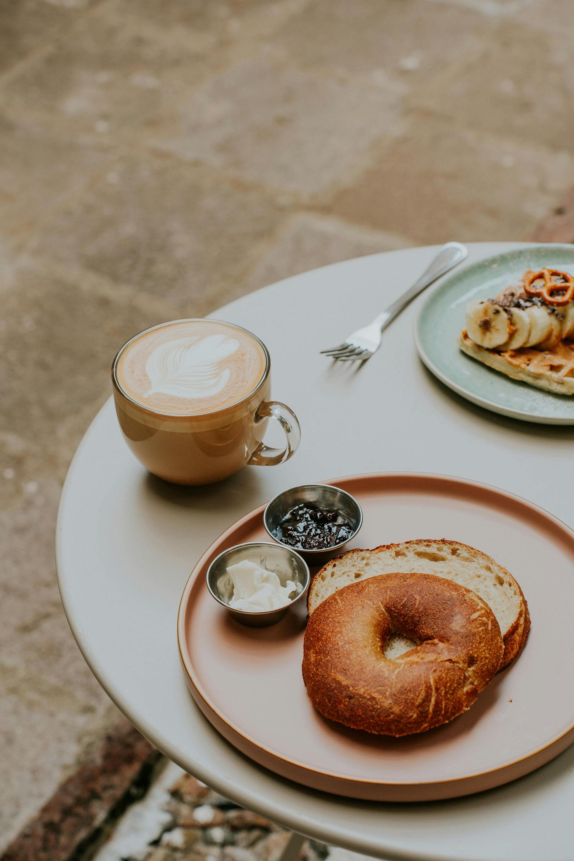 Un tavolo con caffè, un bagel con formaggio cremoso e guarnizioni e waffle.