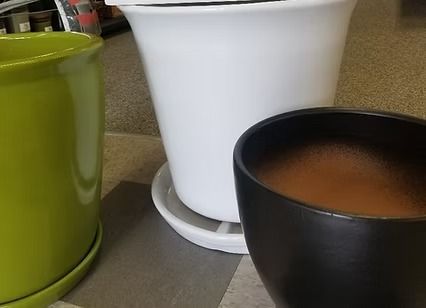 Three mugs on a countertop: green, white, and black, with the black one filled with coffee.