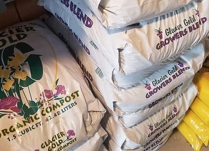 Stacked bags of organic compost and garden soil, mostly white with some yellow bags.