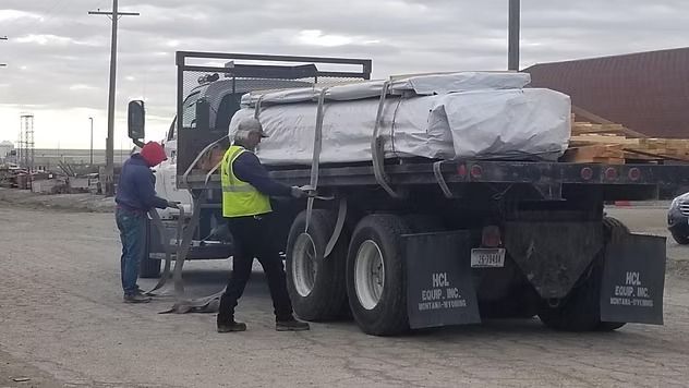 Workers loading a tarp-covered trailer by the roadside under cloudy skies