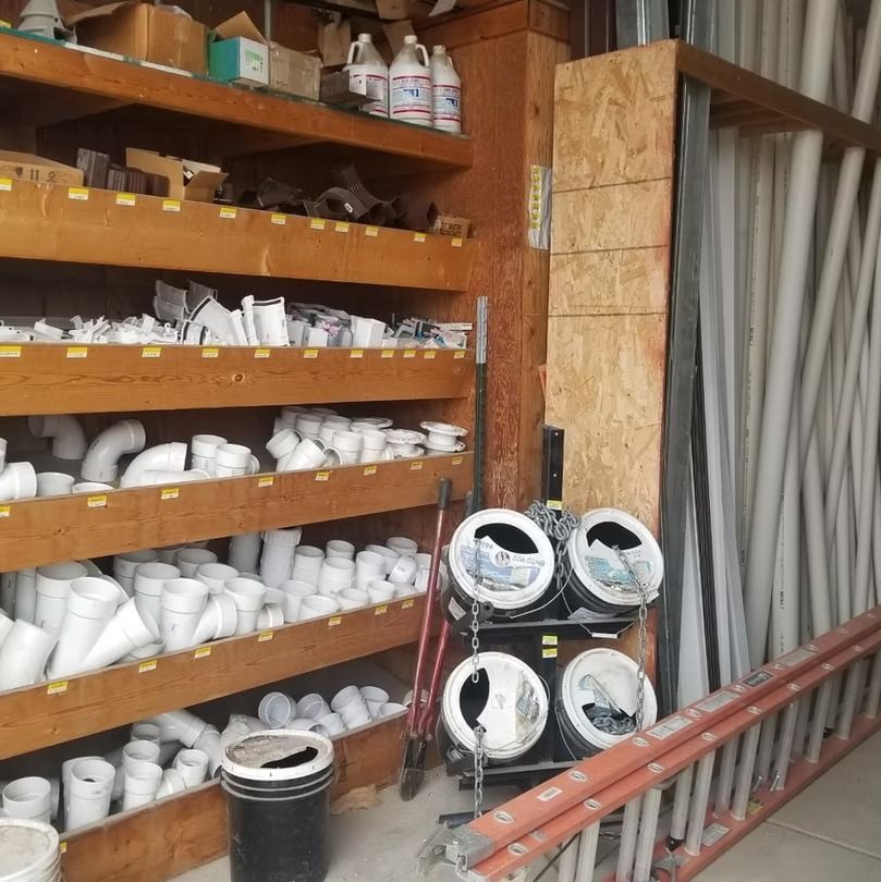 Hardware store aisle with shelves of white PVC fittings and bundled pipes stacked on the right