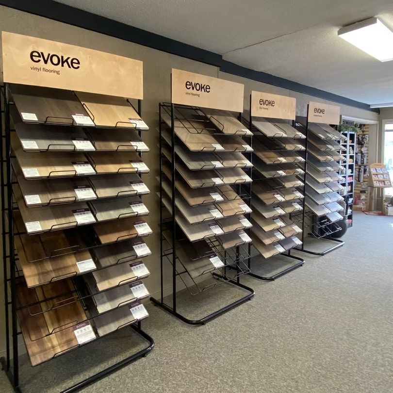 Showroom display racks with sample flooring tiles under Evoke signs in a carpeted store.
