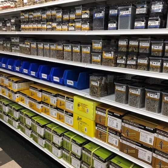 Store aisle with shelves of assorted small packaged hardware bins in blue, green, yellow, and black.