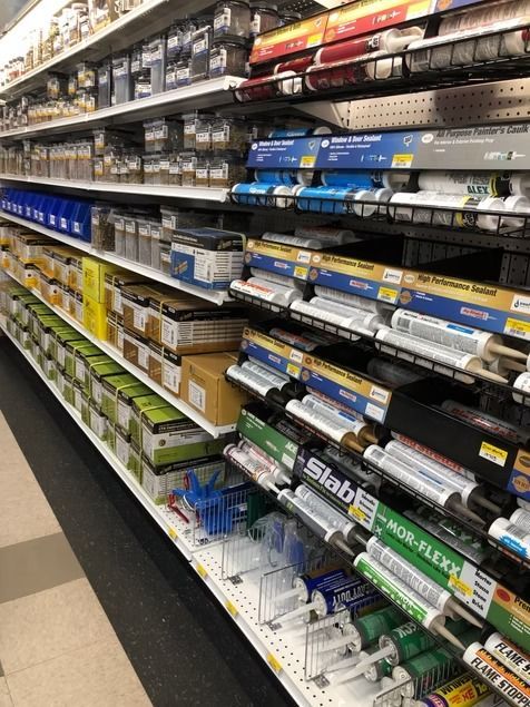 A store aisle lined with rows of boxed and tube hardware supplies on metal shelves.
