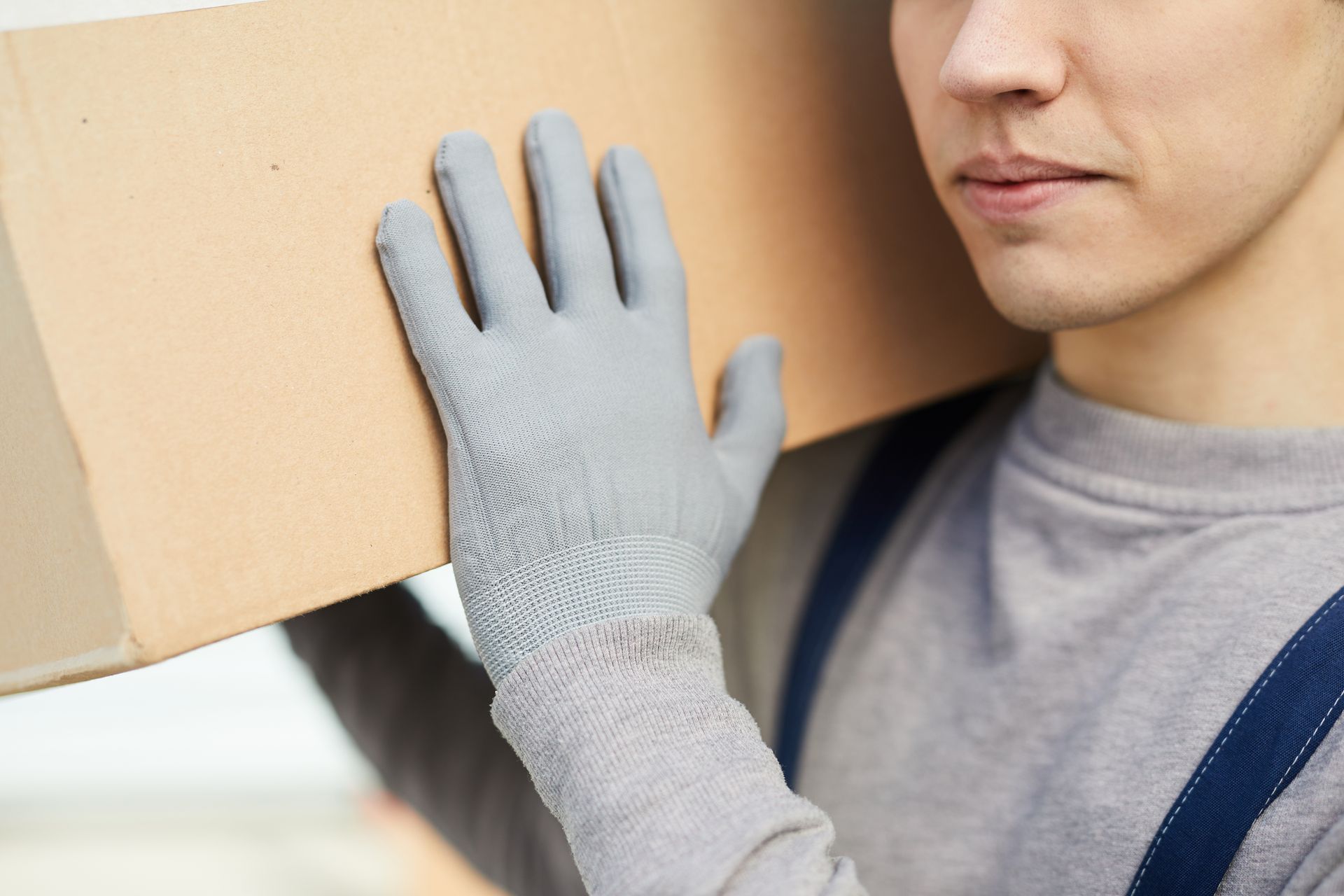 Personne portant une boîte en carton sur l'épaule, portant des gants gris et une chemise grise.