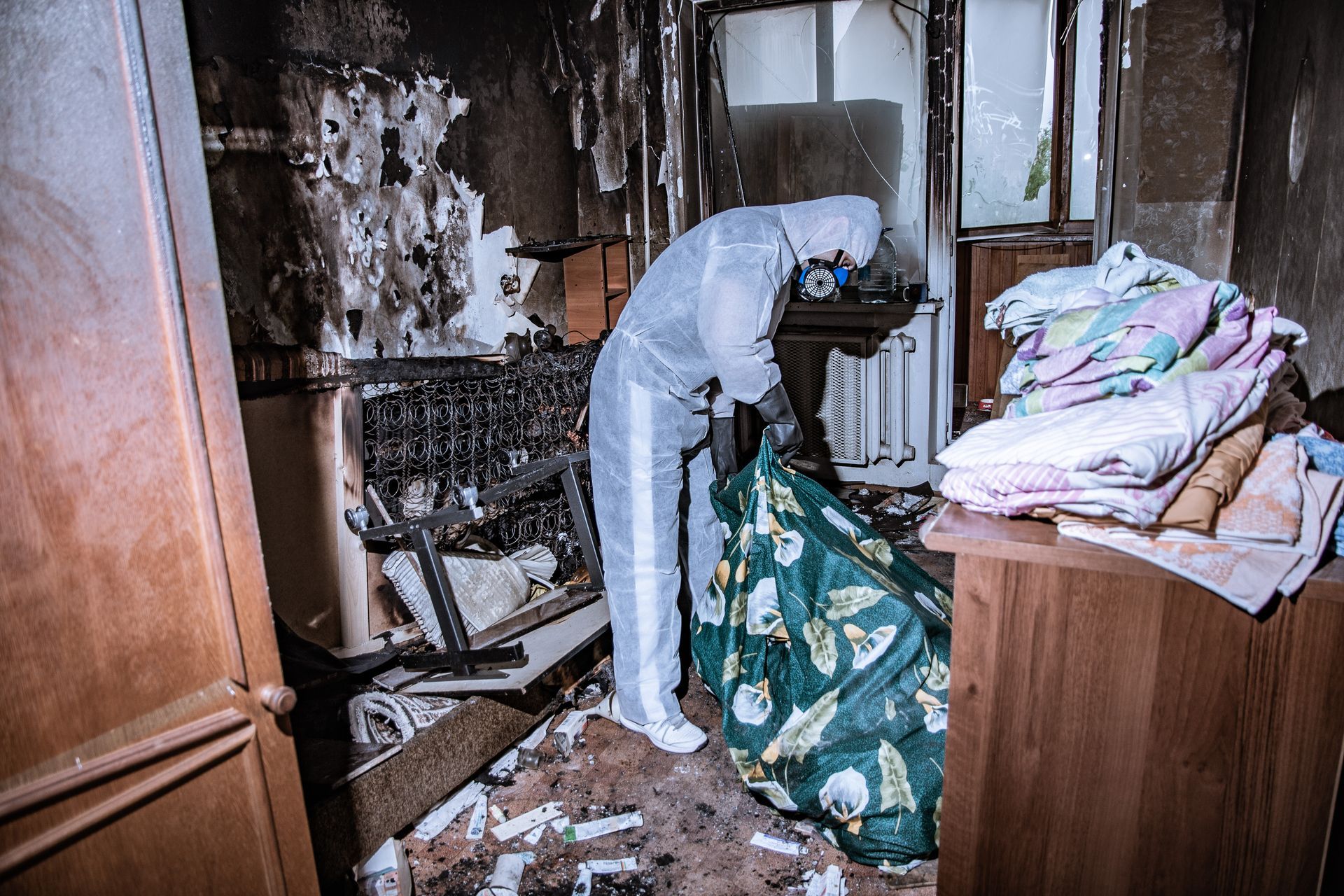 Une personne en combinaison de protection nettoie une pièce fortement endommagée par un incendie.