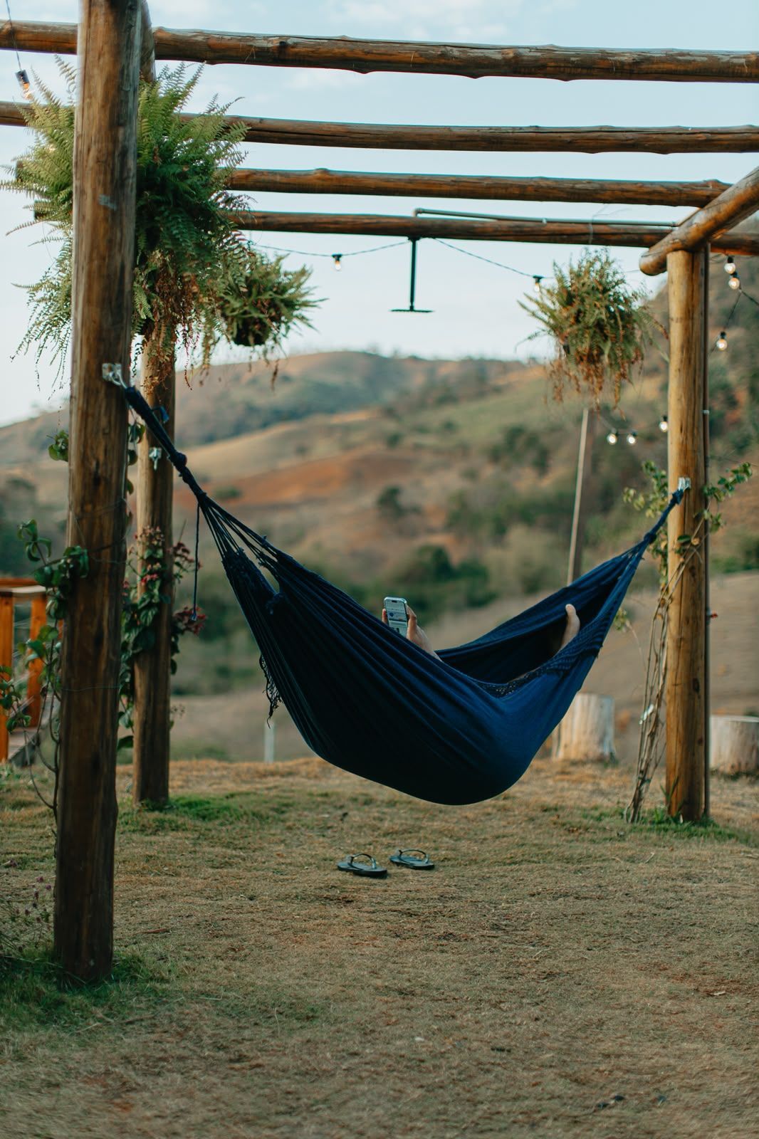 Rede escura pendurada sob uma pérgola rústica de madeira em um campo ao ar livre.