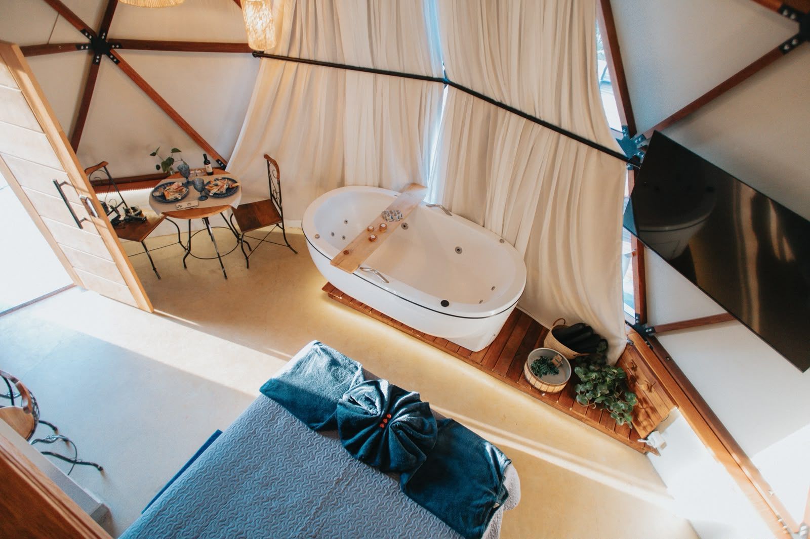 Interior aconchegante em forma de cúpula com banheira branca, cama, escrivaninha e cortinas em tons de madeira quente.