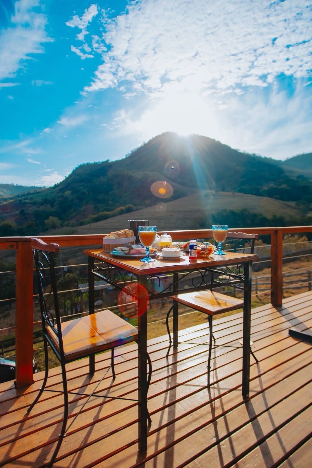 Mesa de café da manhã na varanda ensolarada com vista para as montanhas sob um céu azul brilhante.