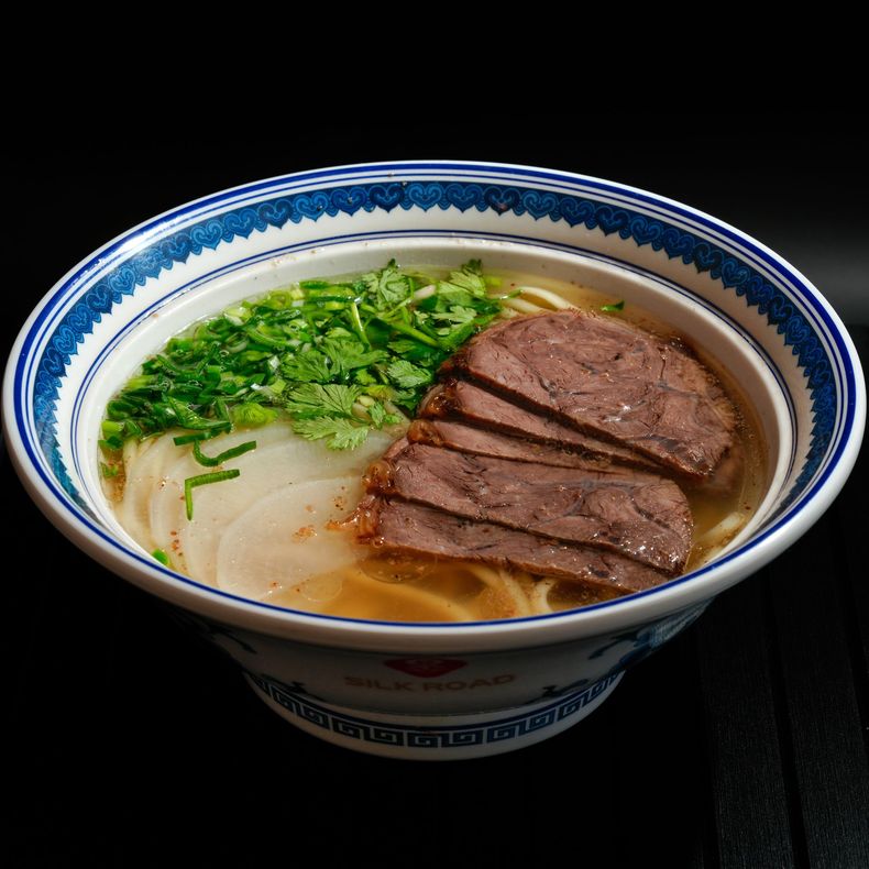Bowl of ramen topped with sliced beef and chopped green onions in a blue-and-white bowl