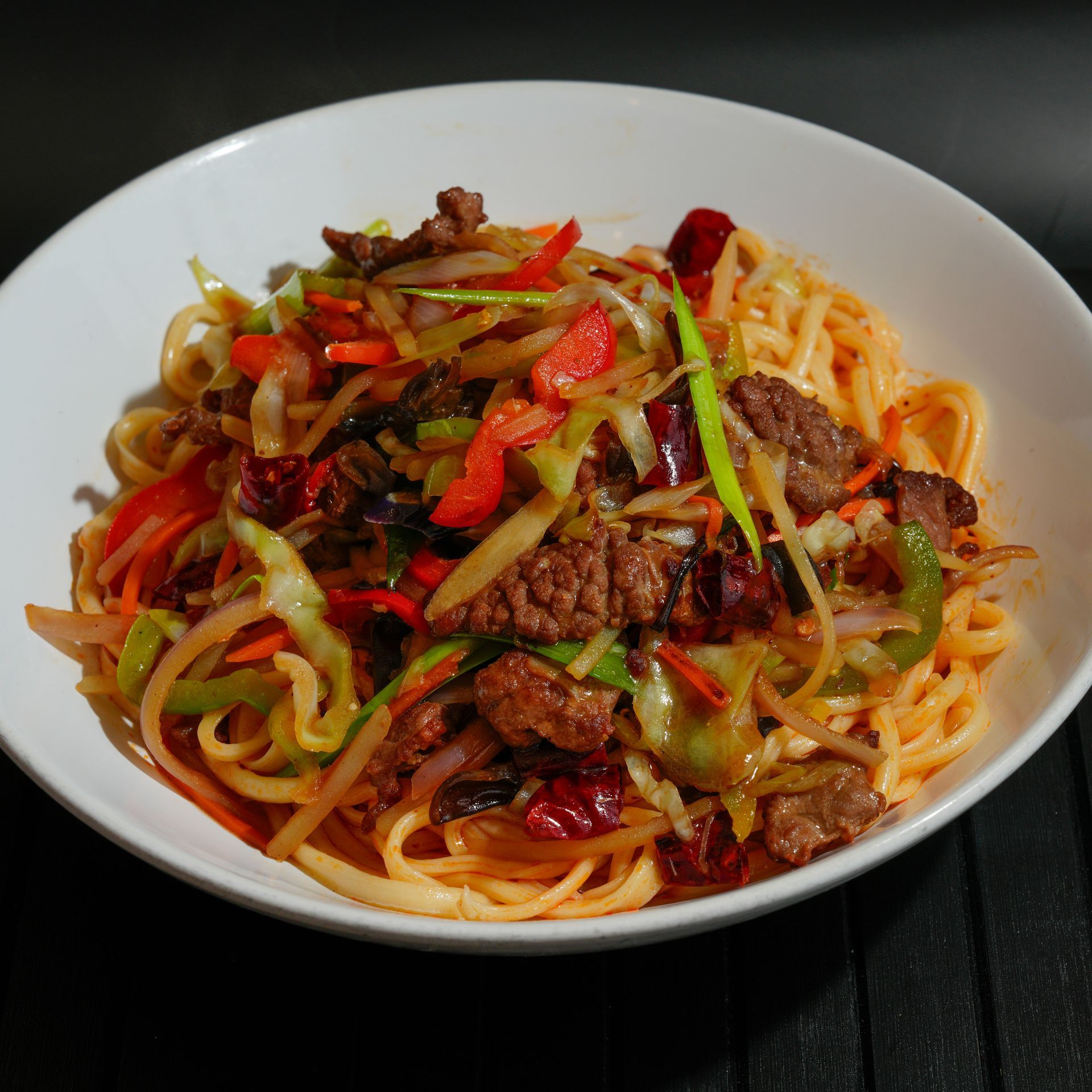 A bowl of spaghetti topped with beef, peppers, and vegetables in a red sauce