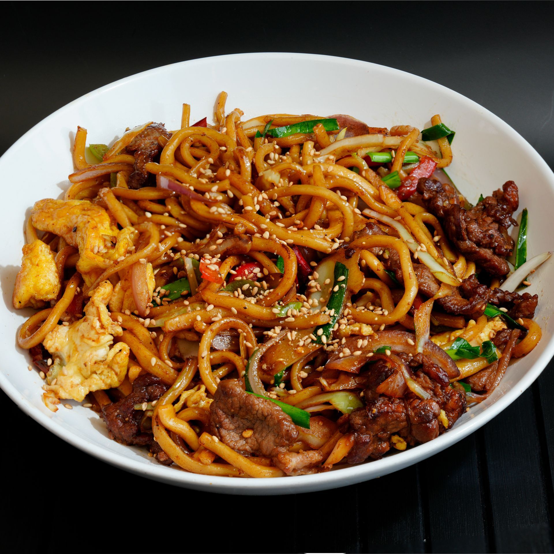 Bowl of stir-fried noodles with beef and egg on a black surface